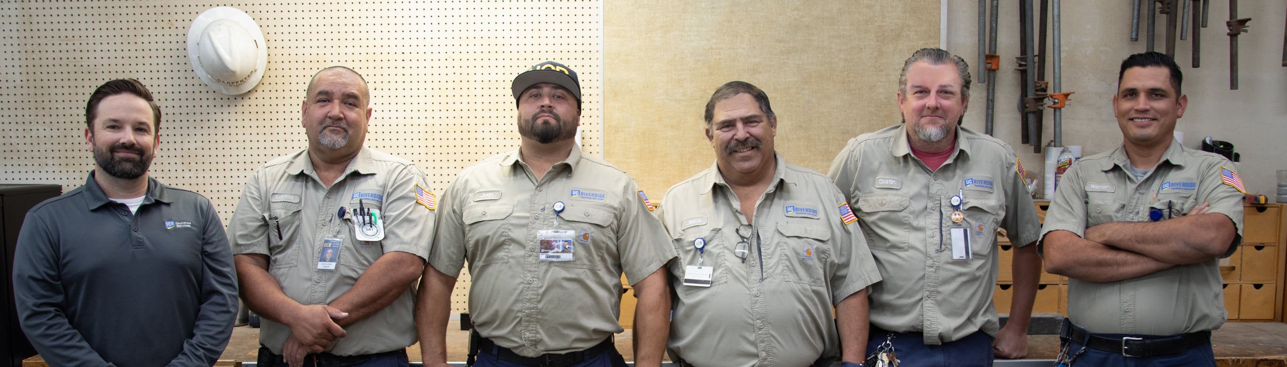 Six workmen in front of cabinets and corkboard