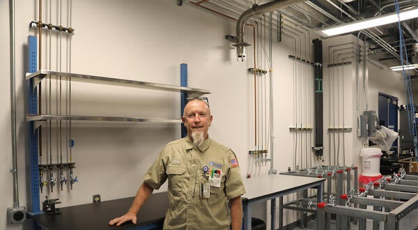 A technician standing inside a clean laboratory with overhead piping and wall-mounted valves