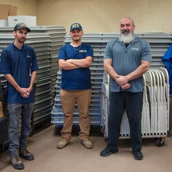 People standing in front of stacked tables, chairs, and dolly equipment