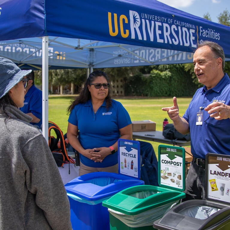 People at an outdoor booth showcasing recycling, composting, and trash bins