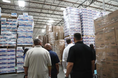 People looking at packaged paper products stacked in a warehouse