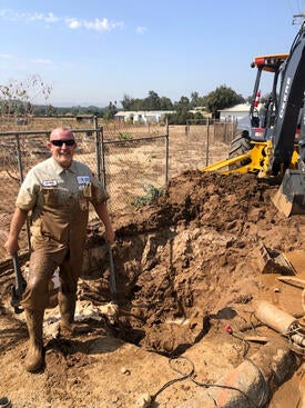 Excavation work at an agricultural site, with a worker standing beside a deep trench